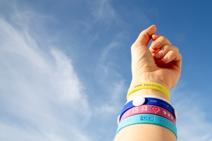Bunte PVC Festival-Armbänder am Handgelenk unter blauem Himmel bei 1a-rubber.de