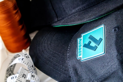 Gummipatch mit 1a-rubber.de Logo auf Kappe genäht – Maßband und Garn im Hintergrund