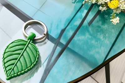 Schlüsselanhänger aus PVC in Blattform, strukturiertes Design auf Glasfläche mit Blumen.