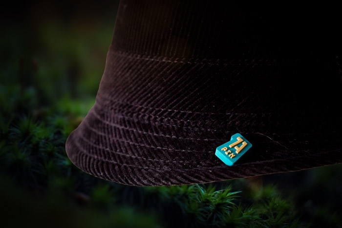 Schwarzer Hut mit 1A Rubber Pin auf dunklem, moosbewachsenen Untergrund – Elegantes Design für Business und Events