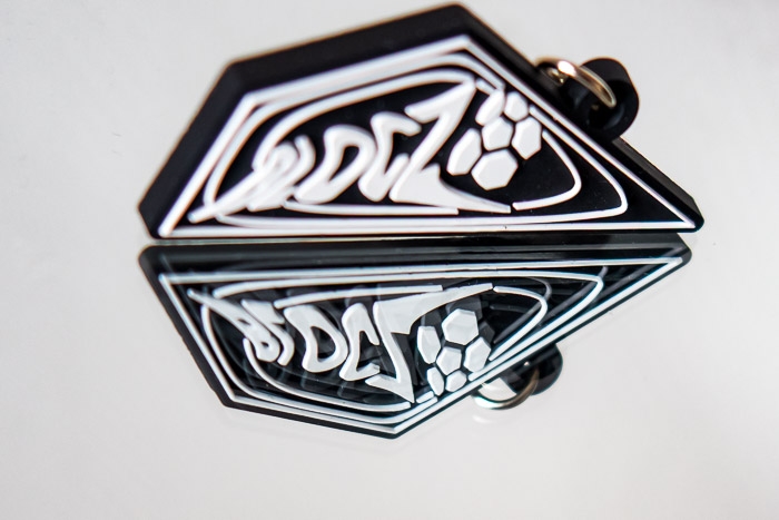 Schwarzer PVC-Schlüsselanhänger mit stilisiertem Logo & Schriftzug – Hochwertiges individuelles Design.