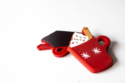 Zwei rote weihnachtliche Gummi-Magnete in Form einer Tasse mit heißem Getränk und einer Schiefertafel an Magnetwand.