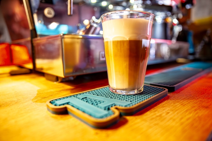 Latte Macchiato auf individuell gestalteter Barmatte neben einer Espressomaschine – Barzubehör für Cafés, Bars und Restaurants.
