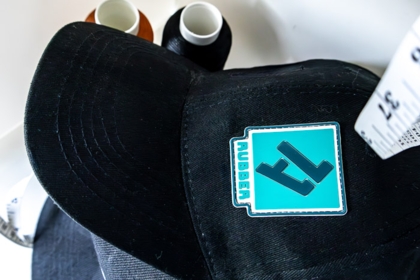 Schwarze Cap mit aufgenähtem 1a-rubber.de Patch und Garnrollen im Hintergrund
