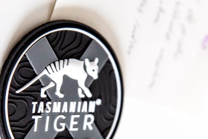 Nahaufnahme eines runden schwarzen Gummi-Magneten mit Tasmanian Tiger-Logo und geprägtem Design hält ein Blatt Papier.