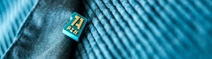 1A Rubber-Pin mit blauer und goldener Logo auf einem dunklen Kordstoffhintergrund