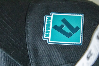Aufgenähter 1a-rubber.de Patch auf schwarzer Cap mit Maßband im Hintergrund