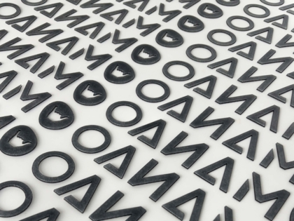 Mehrere schwarze 3D PVC-Applikationen mit Logoformen auf Trägerfolie – 1a-rubber.de