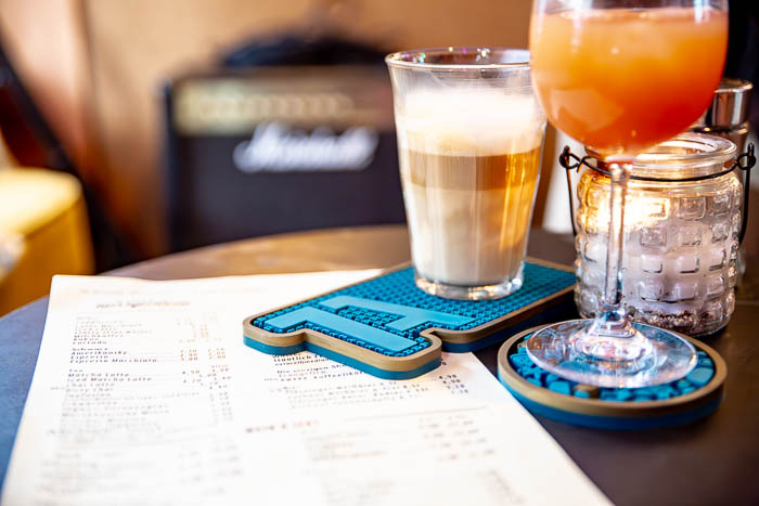 Stilvolle Barmatte mit 1A-Logo, serviert mit einem Latte Macchiato und einem Cocktail in einer gemütlichen Bar-Atmosphäre.